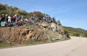 Spectators gathered in support of rally drivers cheering on the side of the road.