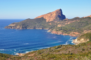 Red cliffs of the Capu Rossu summit plunging into clear waters of the Mediterranean sea in Corsica.