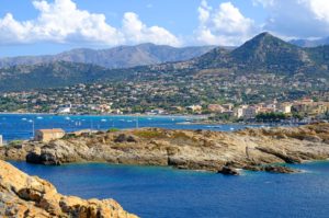 The idyllic setting of L'Ile Rousse by the sea backed by hills and lush vegetation.