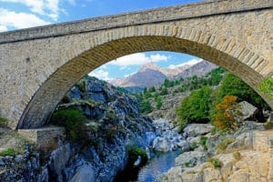 Corsica's highest mountain peaks towering over river flowing in rocky granite canyon.