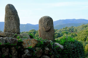 Prehistoric statue-menhirs exposed side by side on granite rocks in front of green hills of the Gulf of Valinco.