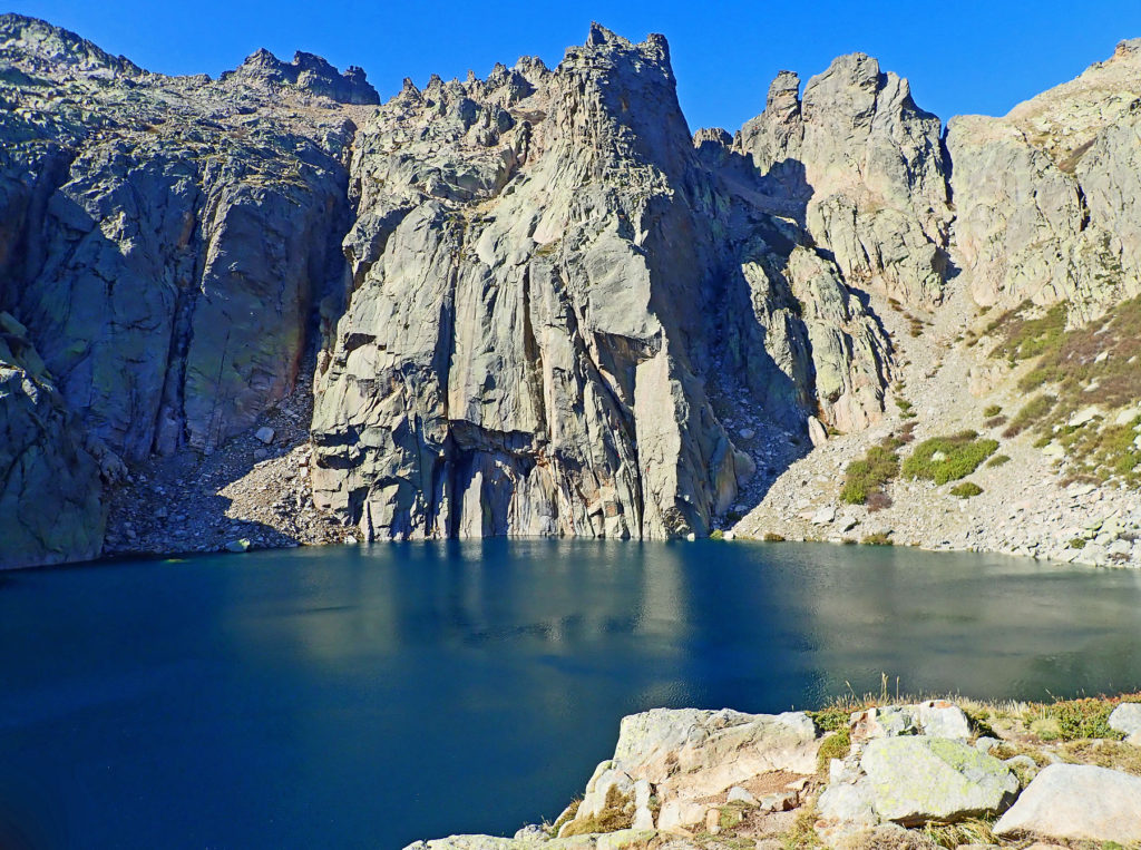 Tall granite walls plunge into deep blue waters of Lac de Capitello.