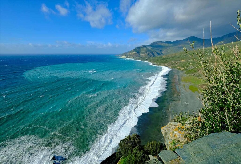 Nonza beach’s contrast of deep blue sea and dark stones creates an unforgettable coastal landscape.