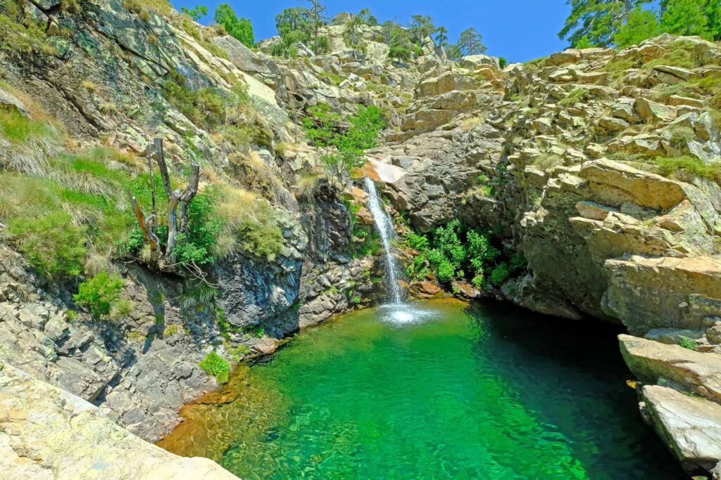 Radule waterfalls plunge 25 meters into stunning emerald pools with high mountains as a backdrop.
