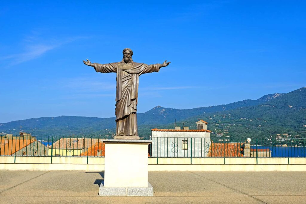 In front of the church, a graceful statue of Jesus extends a protective embrace over Propriano.