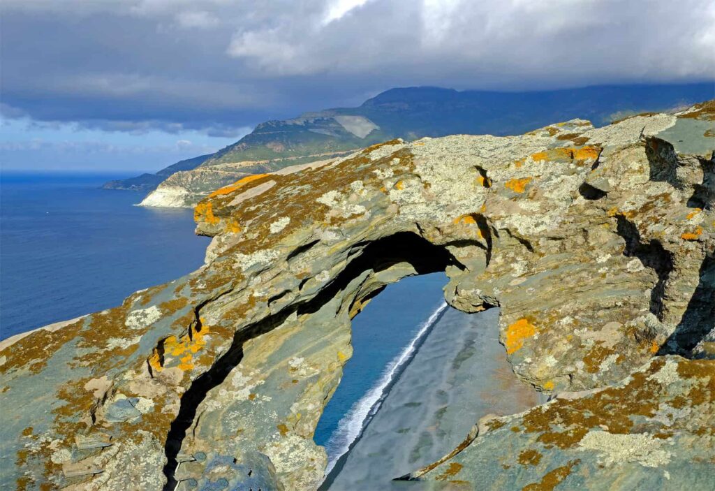 A framed view of Nonza’s shoreline through the Trou du Diable rock formation.